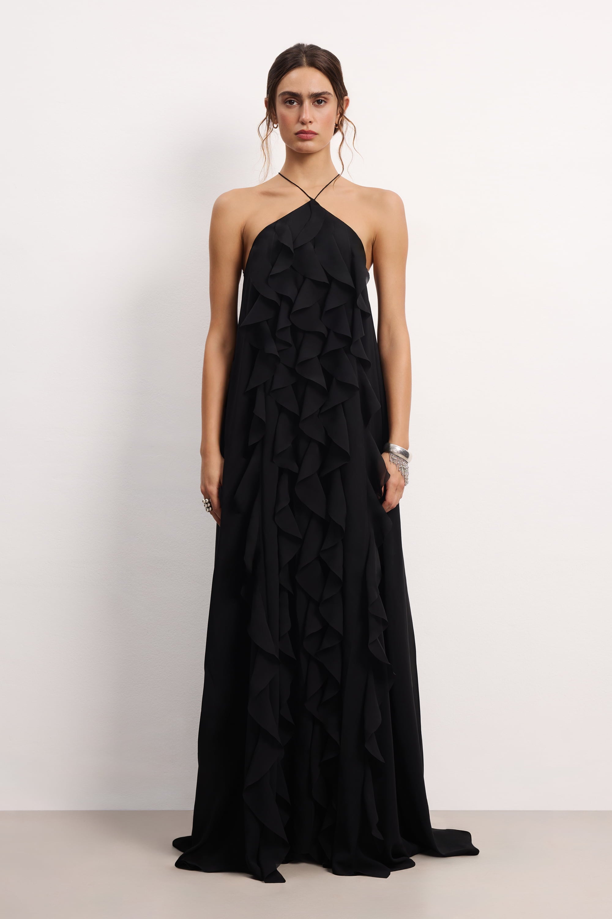 Woman wearing a black halter neck Illusion dress with thin straps and ruffled layers on a white background, front view