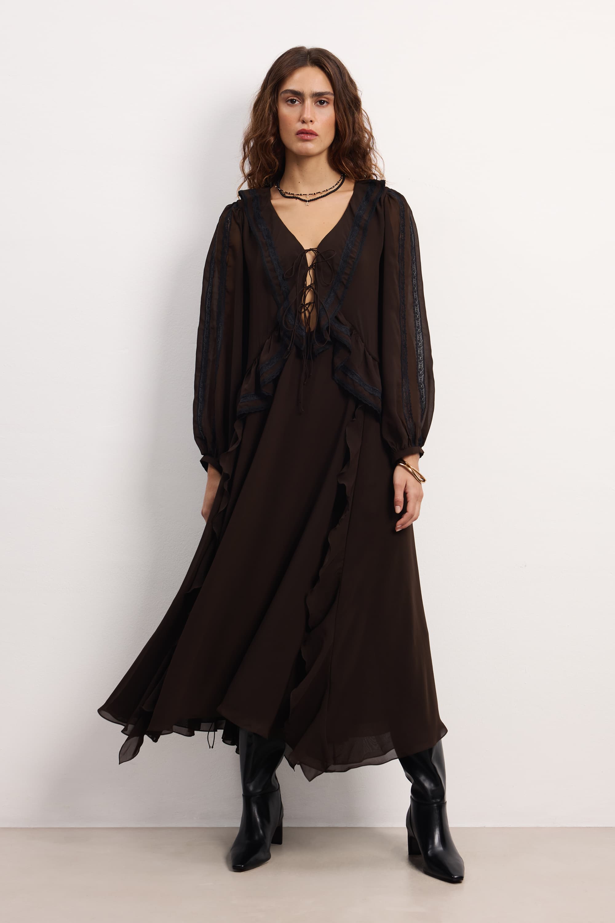 Woman wearing a long black Midnight dress with sheer sleeves against a white background