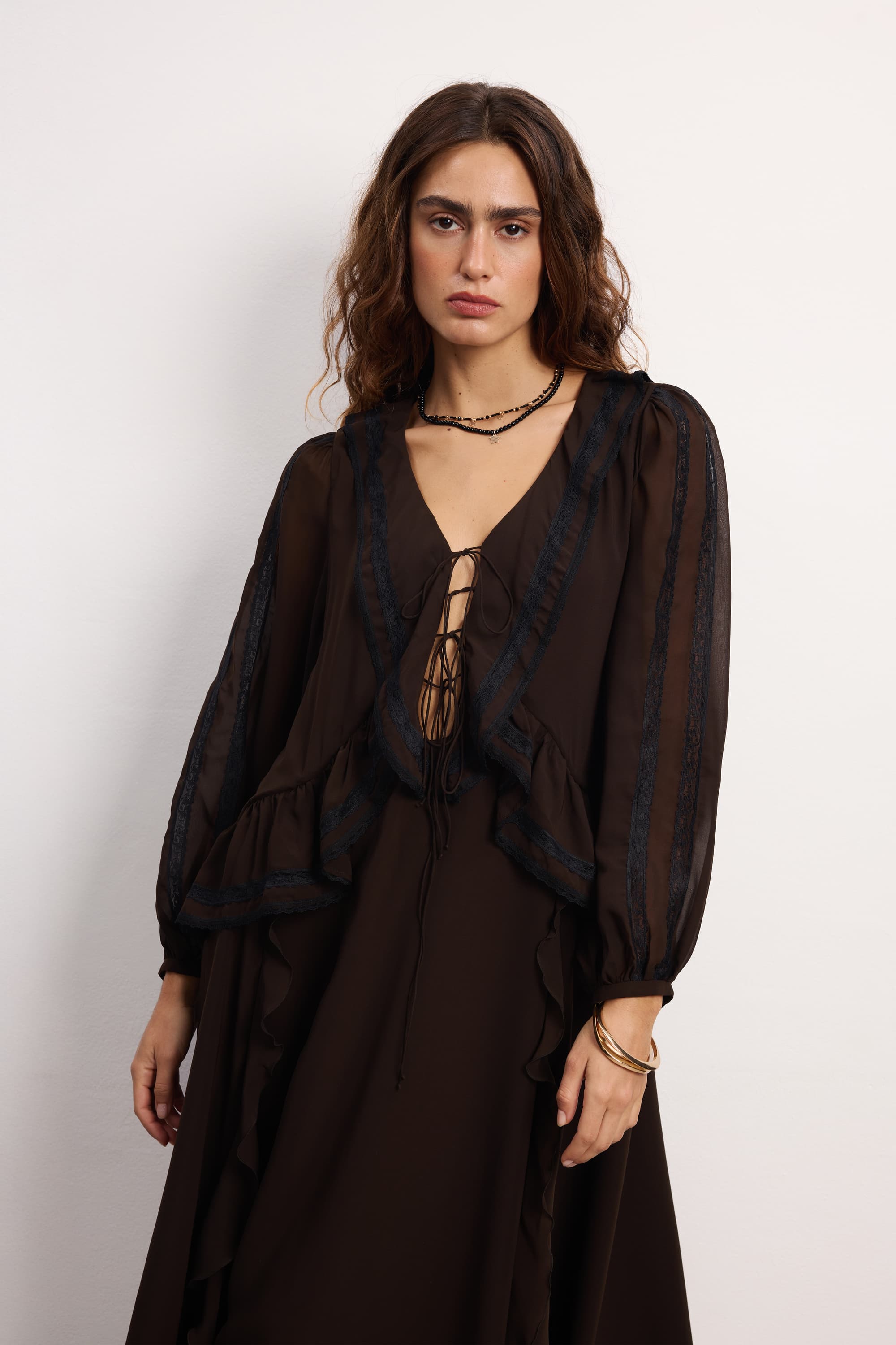 Woman wearing a long black Midnight dress with sheer sleeves against a white background