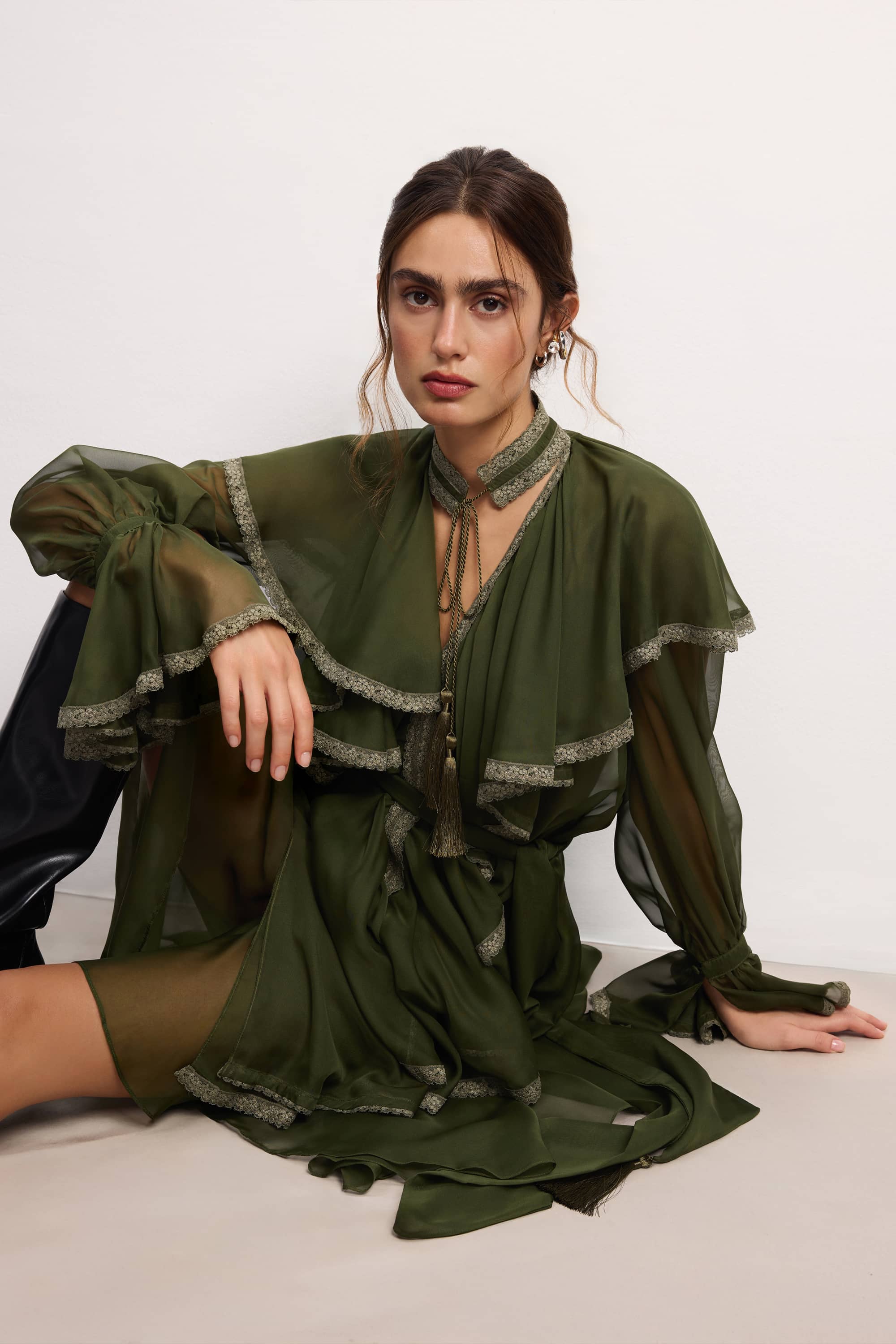 Woman wearing a olive ruffled Ocean Of Tenderness midi dress with black knee-high boots against a white background, front view